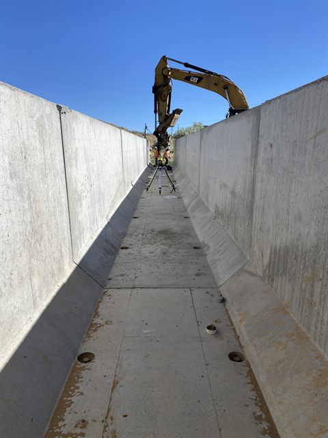 A finished cast-in-place concrete drainage channel, an excavator working above the wall.