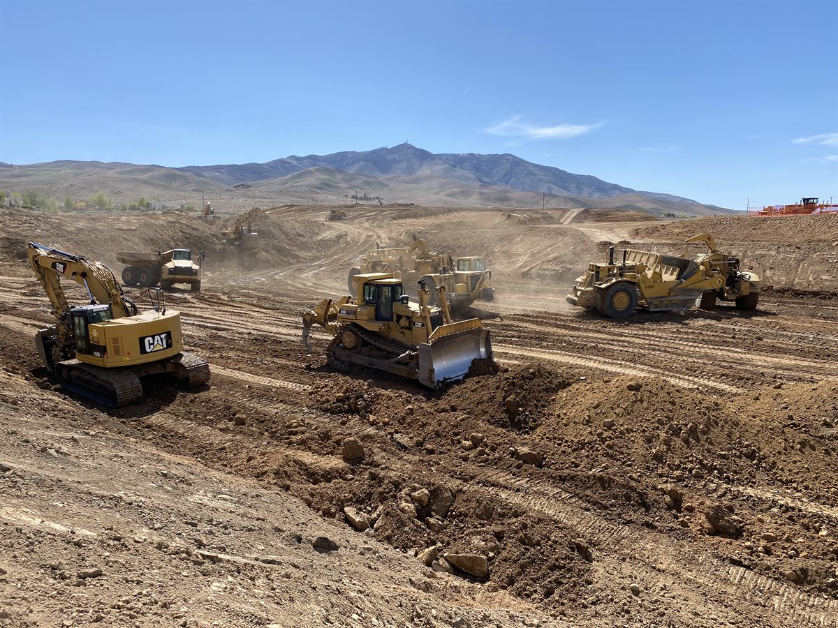 An excavator, a dozer, scrapers and an articulated hauler all working one mass grade below the Nevada hills.