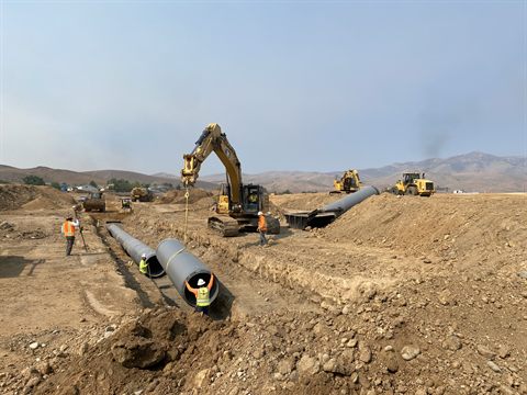 Large-diameter storm pipe being laid into a shored trench, an excavator setting each length.