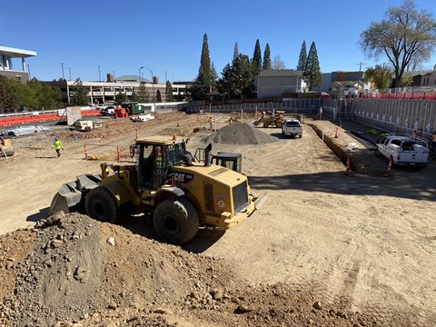 A wheel loader cutting an urban building pad inside shored walls, on a tight downtown site.