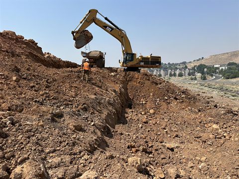 An excavator loading a haul truck on a cut slope above a Reno subdivision.