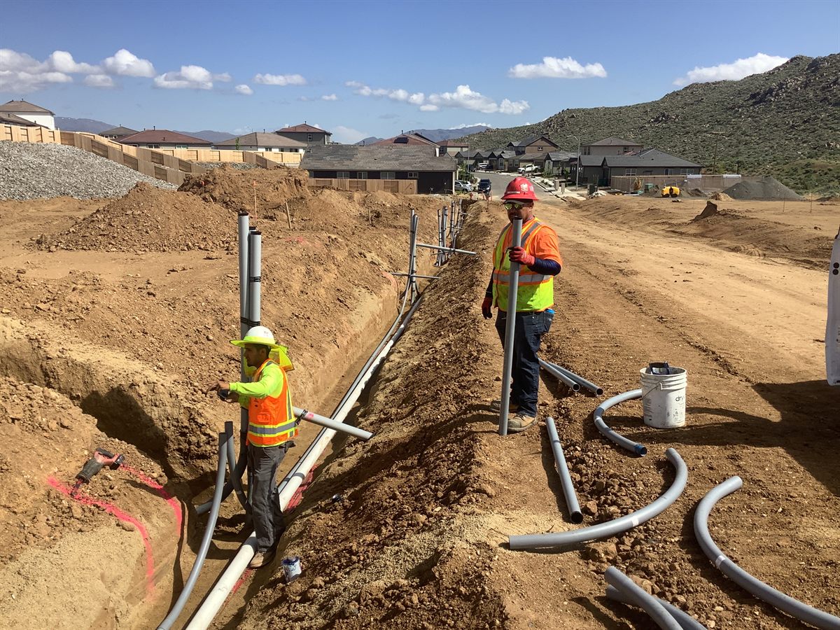 Crew setting conduit and pipe in an open joint trench beside new housing.